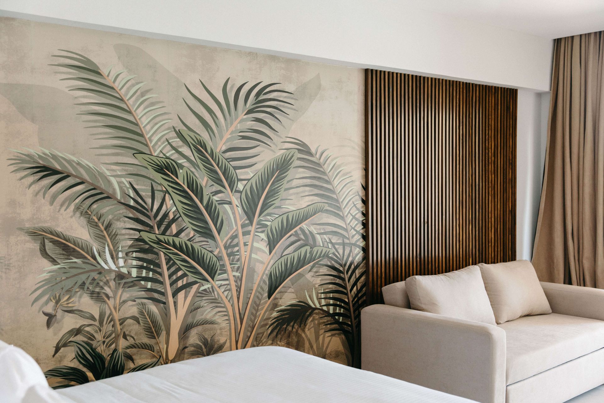 A bedroom with a bed , couch , and palm trees on the wall.