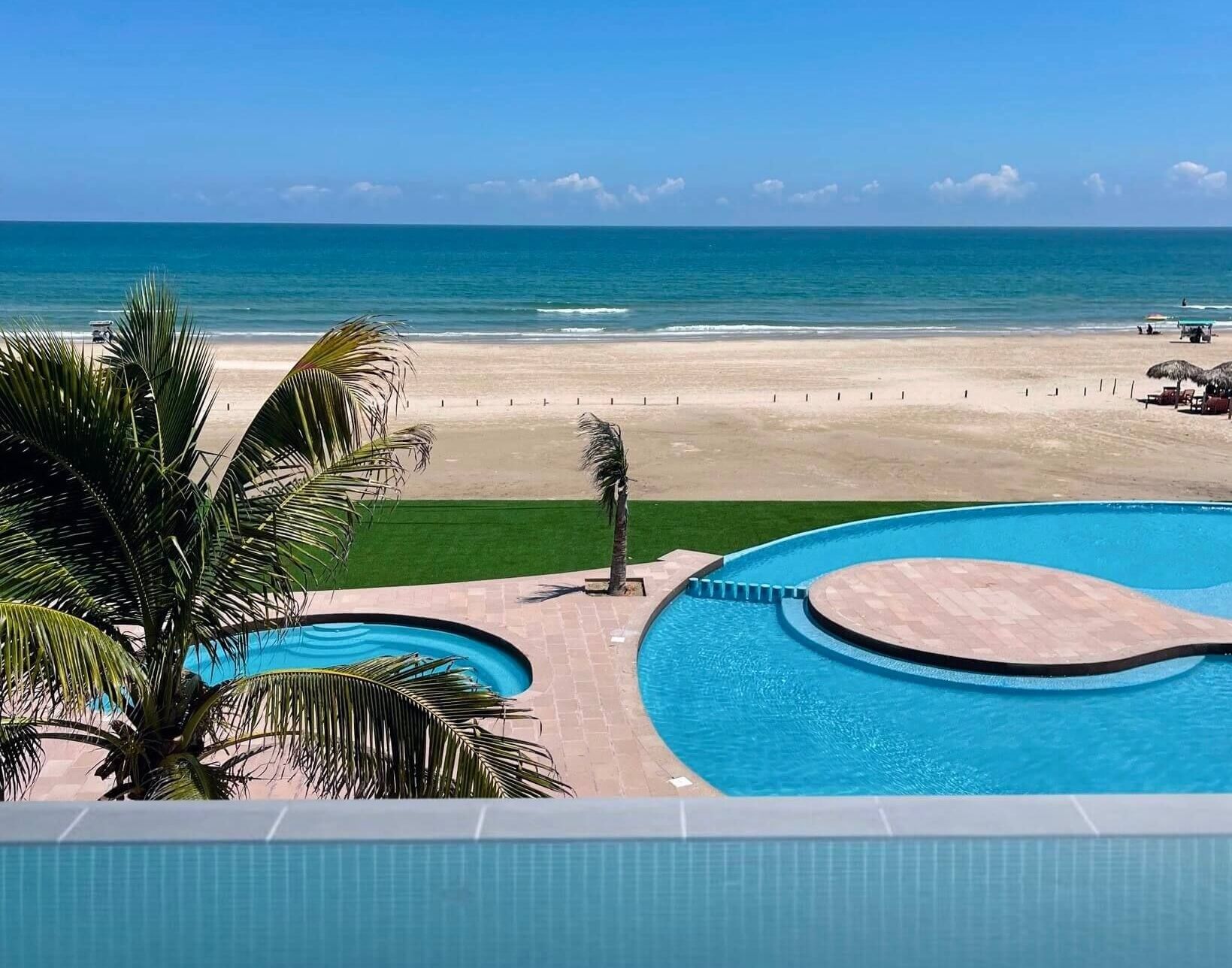 A large swimming pool surrounded by palm trees next to a beach