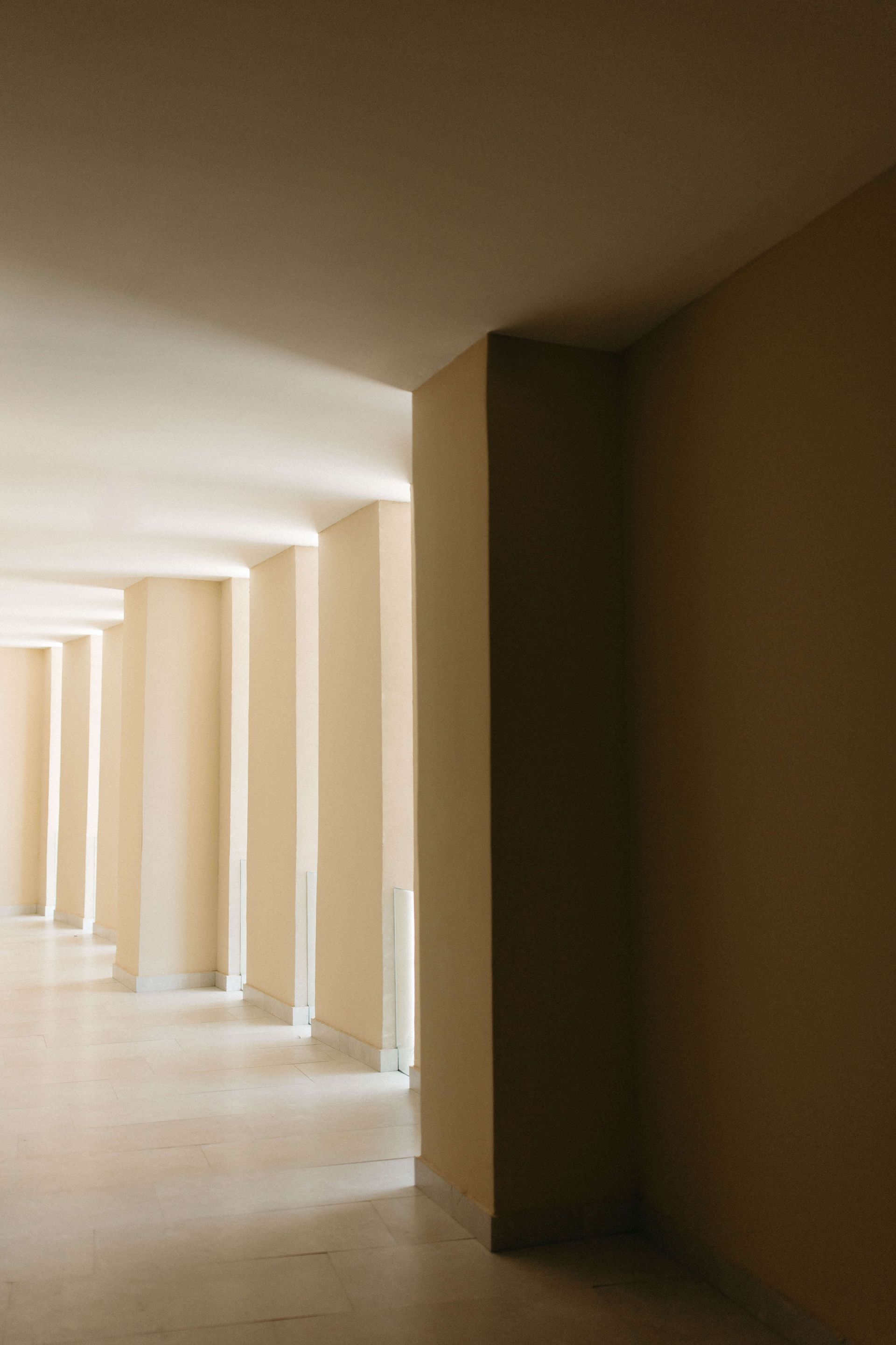 A long hallway with columns and a light coming through the ceiling.