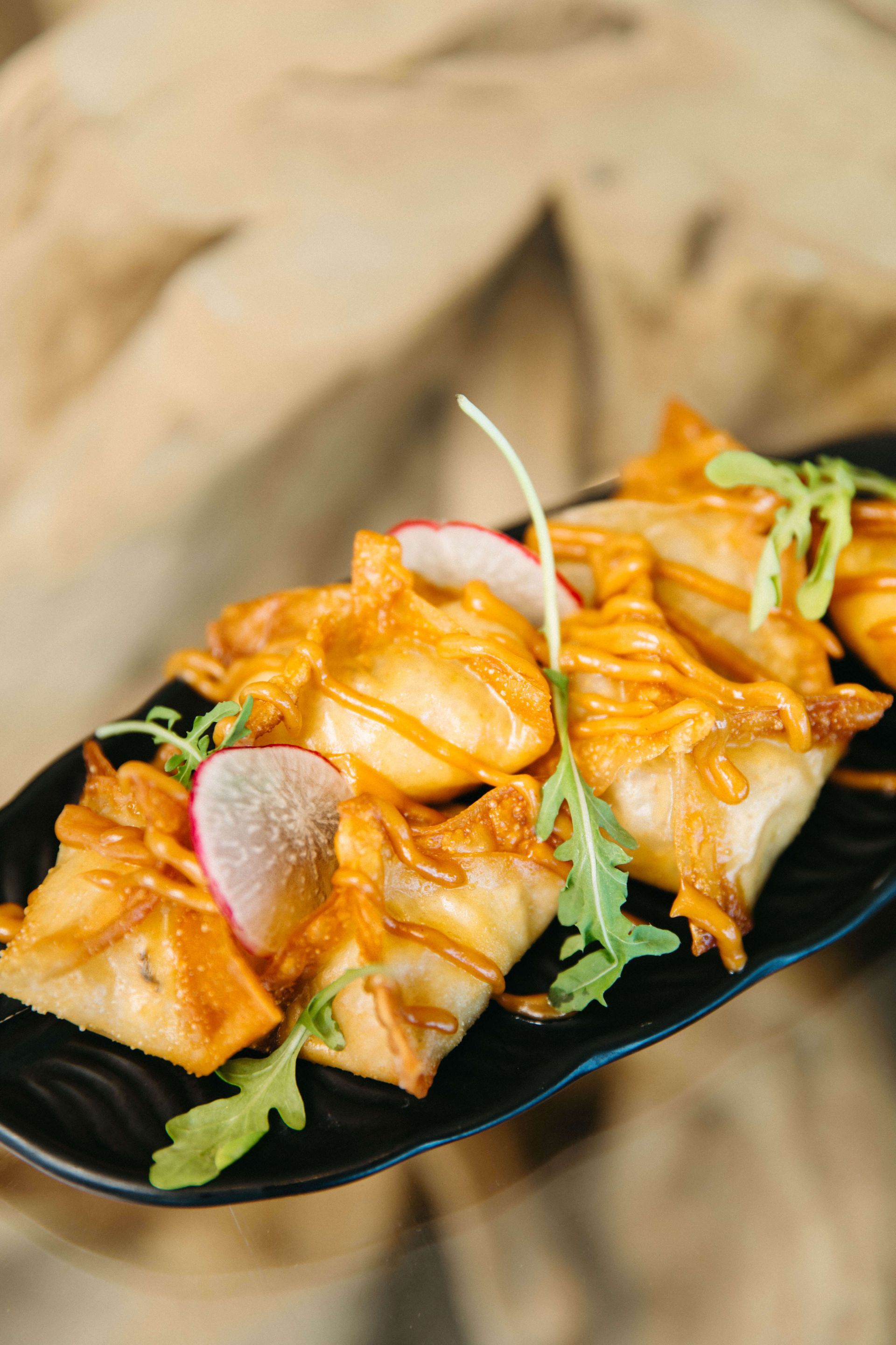 A person is holding a black plate topped with fried food.