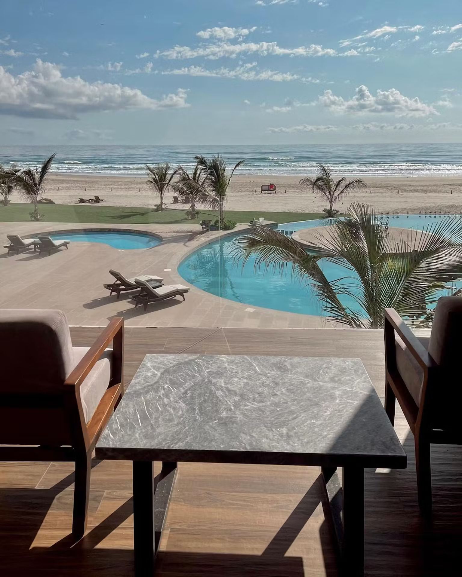 A view of a beach from a balcony with a table and chairs.