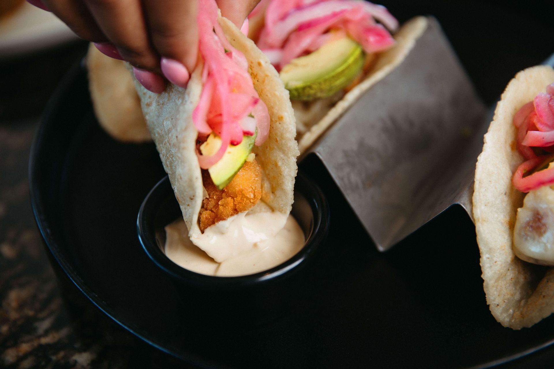 A person is dipping a taco into a bowl of sauce.