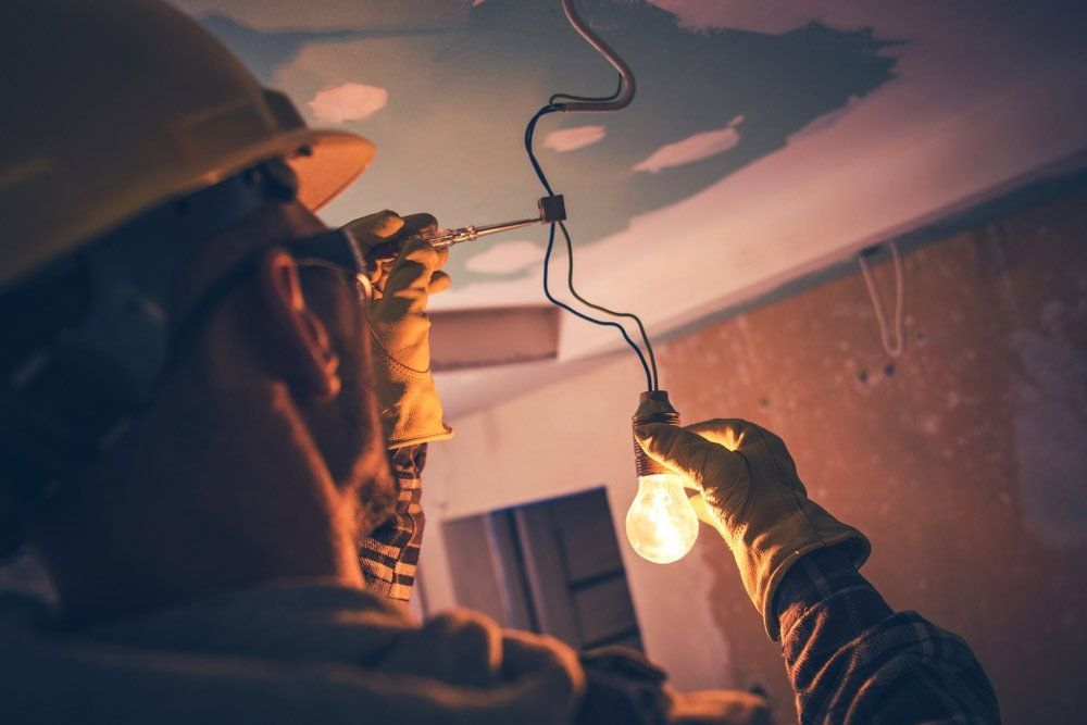 Electrician in a Yellow Hard Hat Installing a Lightbulb — Big Electrics in Redlynch, QLD