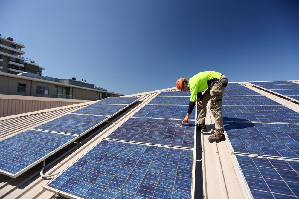 Worker Installing Solar Panels on a Rooftop Under a Blue Sky — Big Electrics in Redlynch, QLD