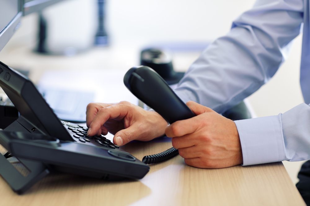 Person Typing on a Black Office Phone, Holding Handset — Big Electrics in Redlynch, QLD
