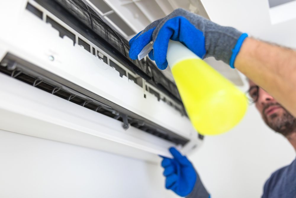 Person Cleaning a White Air Conditioner — CQ Refrigeration Air-Conditioning & Electrical Pty Ltd in Lammermoor, QLD