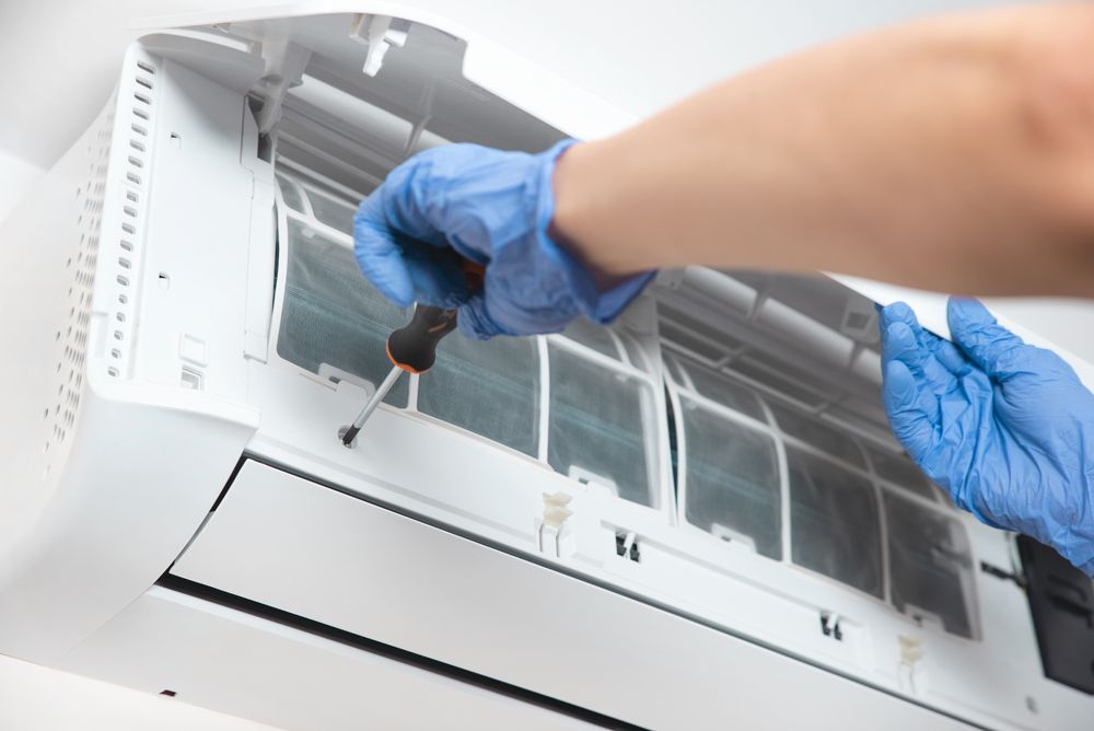 Blue-gloved Hands Cleaning an Air Conditioner Filter — CQ Refrigeration Air-Conditioning & Electrical Pty Ltd In Yeppoon, QLD