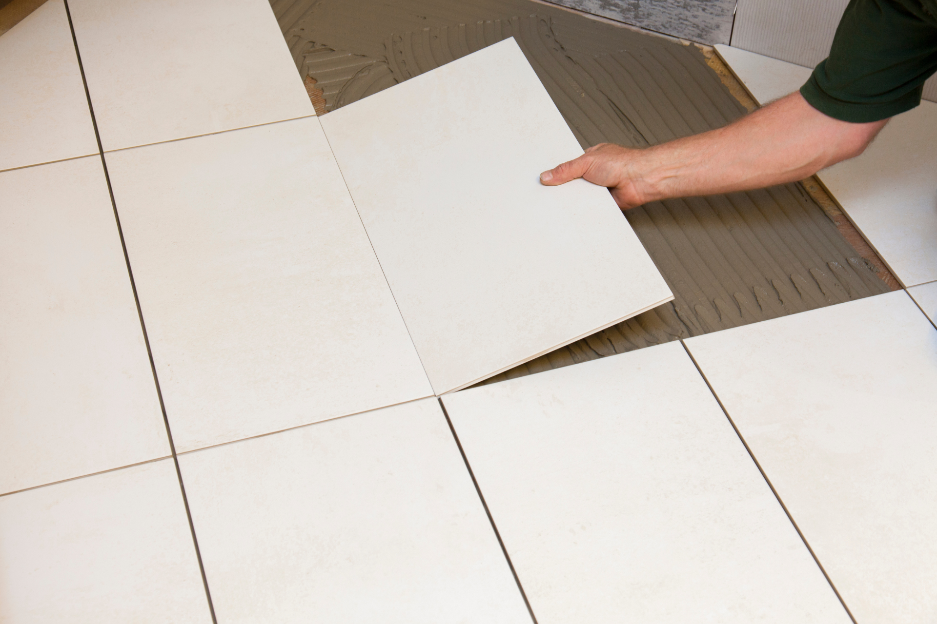 A person is laying a tile on a tiled floor.