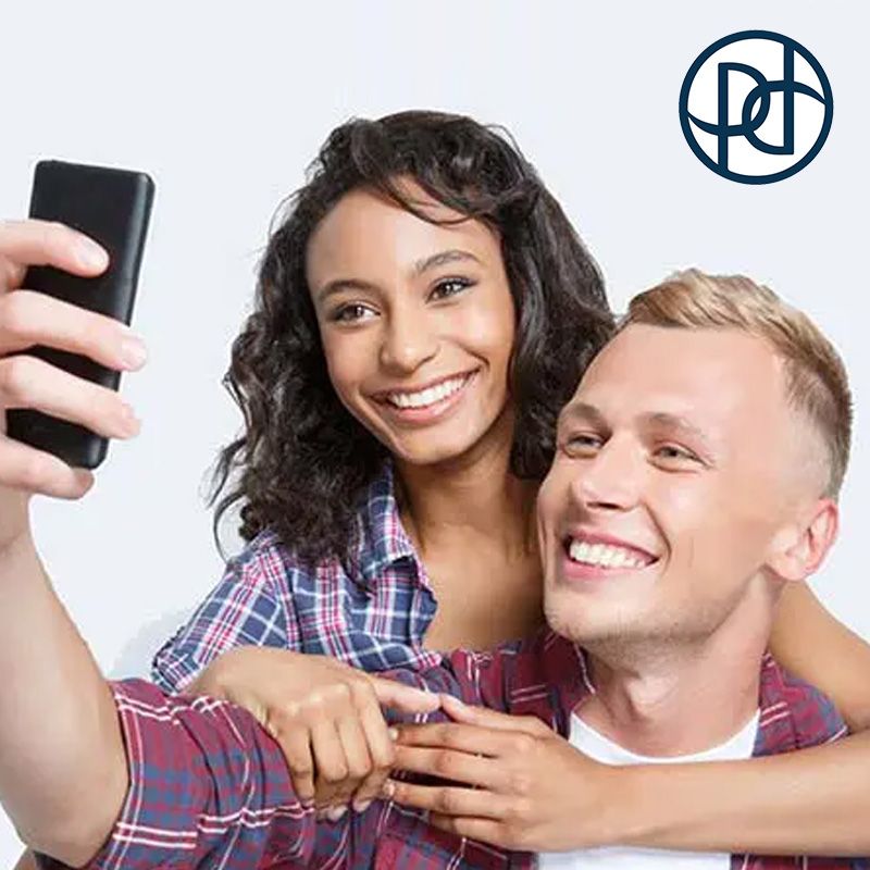 Smiling couple taking a selfie; woman has arm around man's shoulders, both wearing plaid shirts.