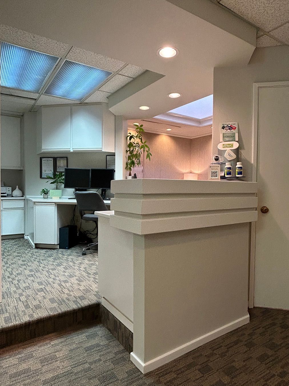Reception desk in an office setting, with a work area in the background and natural light from skylights.
