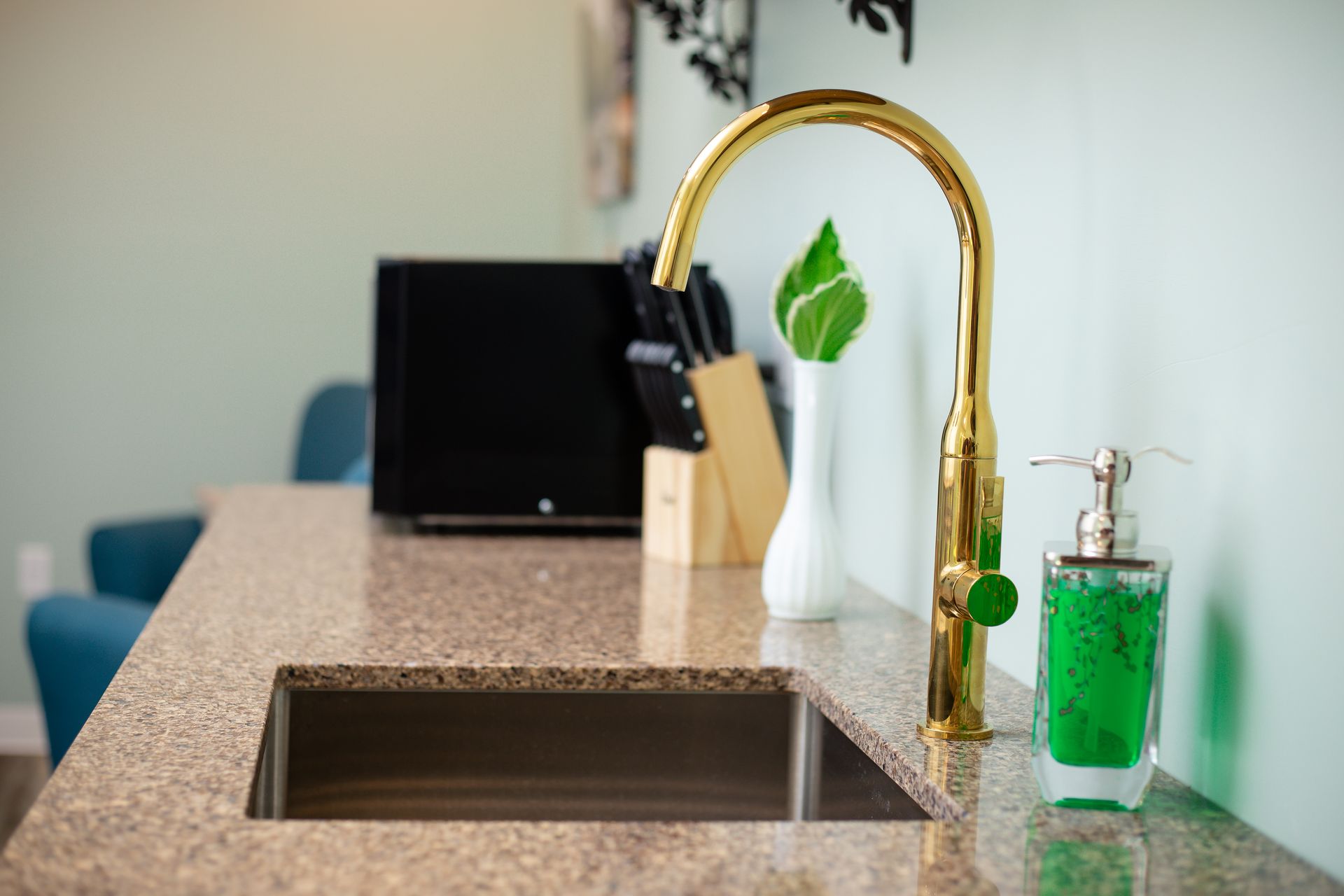 Gold kitchen faucet, granite countertop, stainless steel sink, and green soap dispenser.