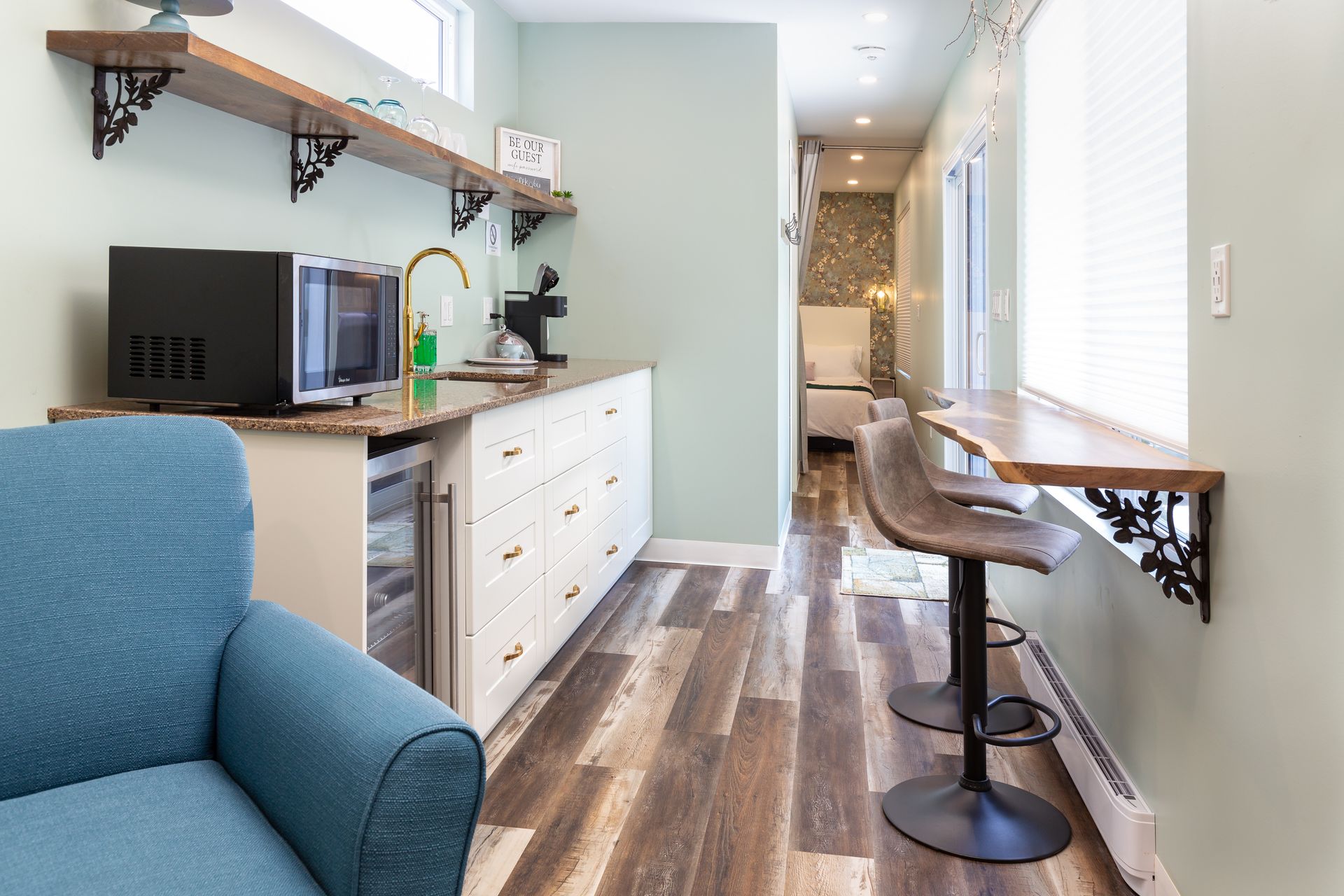 Small, narrow kitchen with counter, microwave, and bar seating. Blue armchair in the foreground.