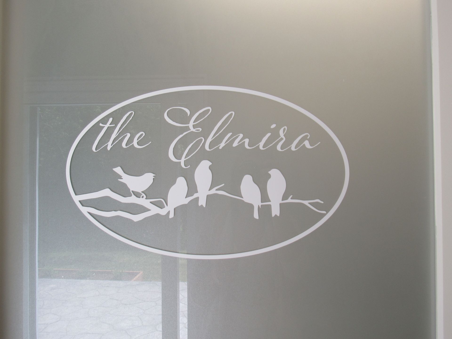 White decal on a glass door with birds on a branch inside an oval that reads 
