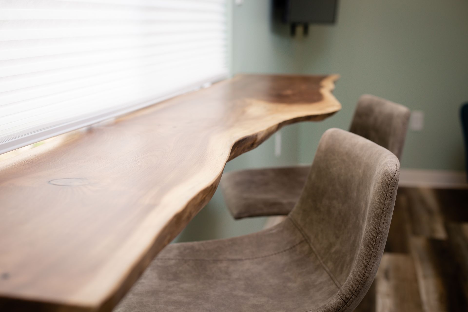 Bar with live edge wooden countertop and two gray upholstered stools near a window.