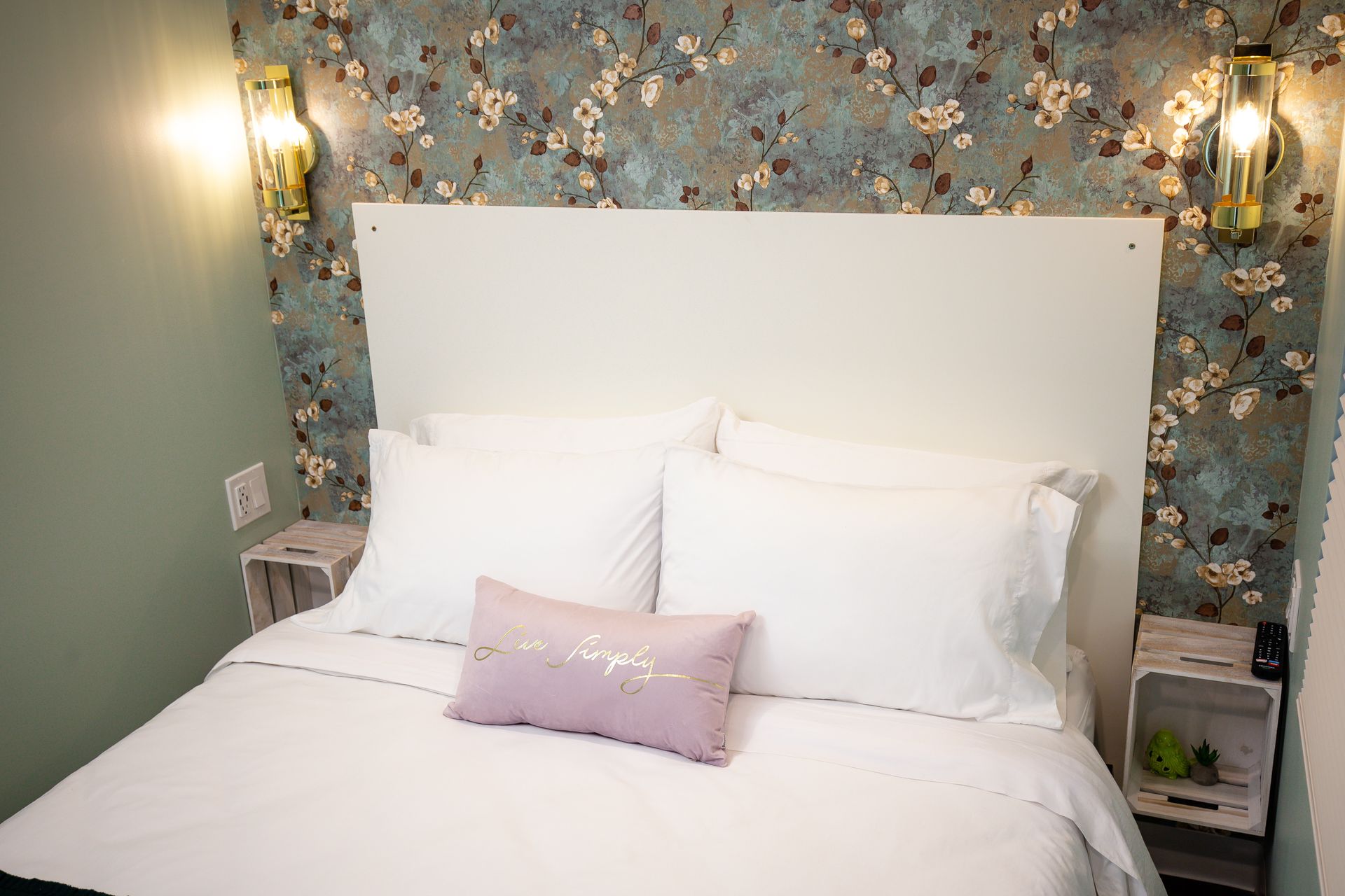 Bedroom with white bedding, floral wallpaper, and decorative wall sconces.