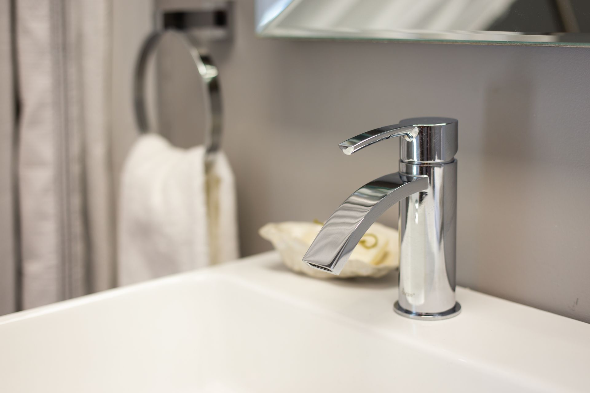 Chrome faucet over white sink with seashell and towel ring.