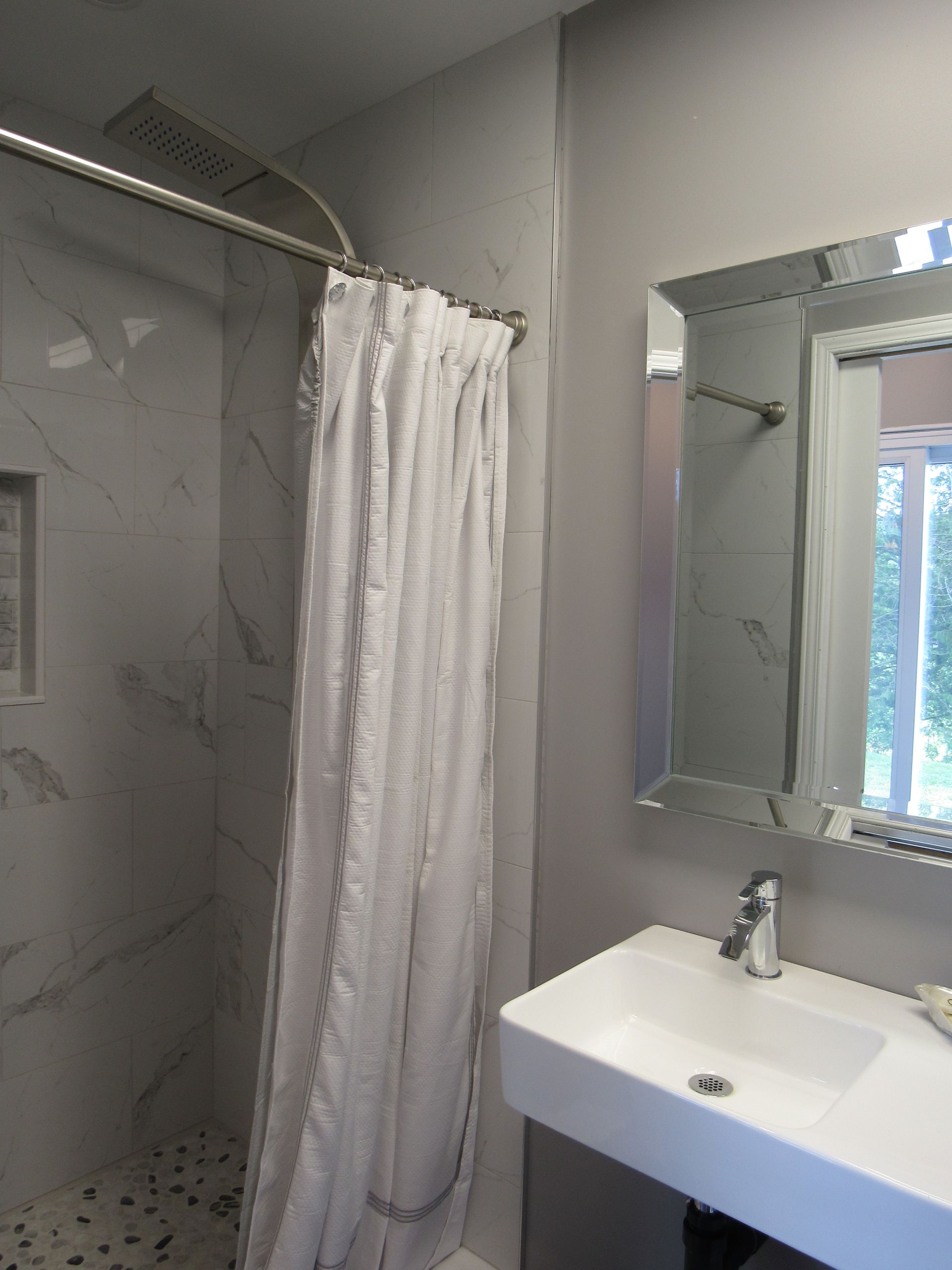 Bathroom with white sink, mirror, marble shower, and shower curtain.