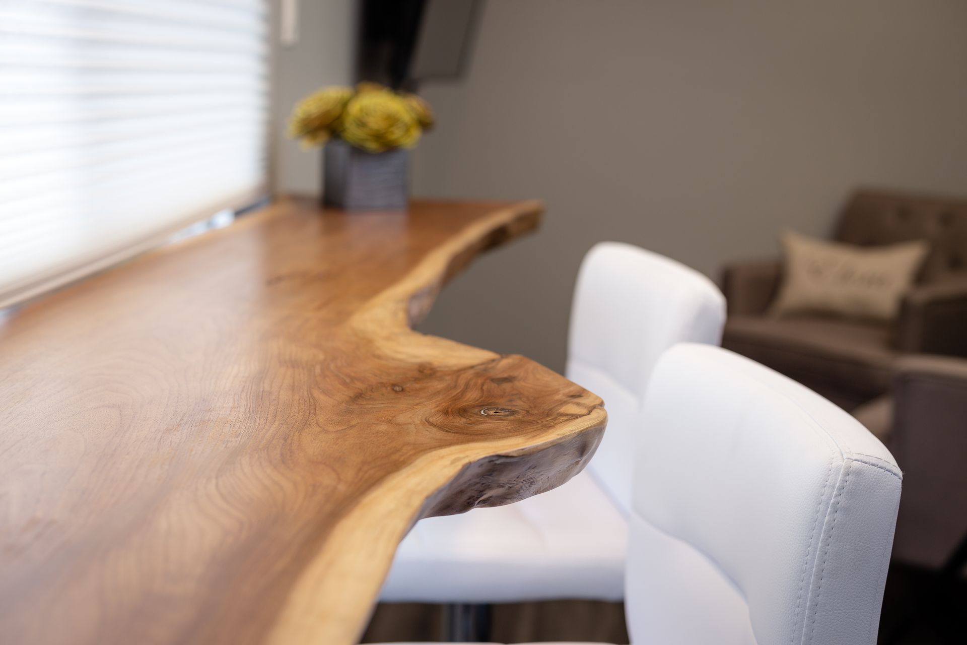Wooden bar with white chairs, window in background.