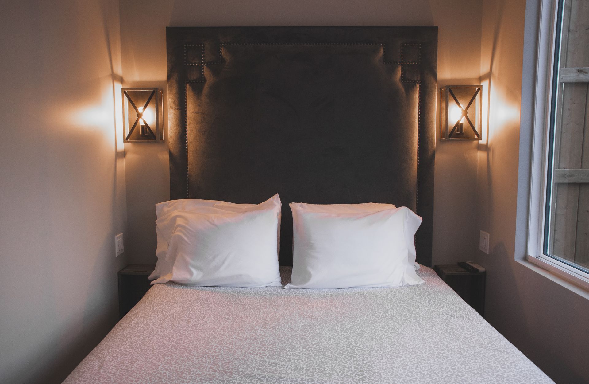 Bed with white pillows, against a dark gray headboard, flanked by sconces, in a bedroom.