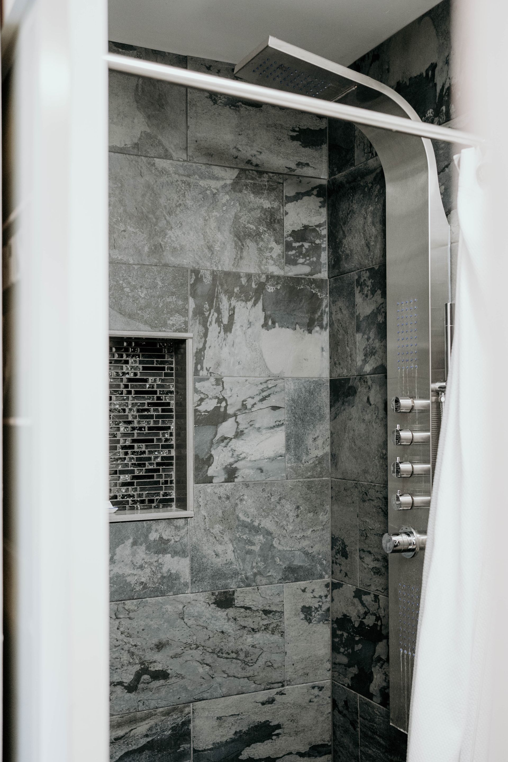 Shower stall with grey stone tiles and a stainless steel shower panel.