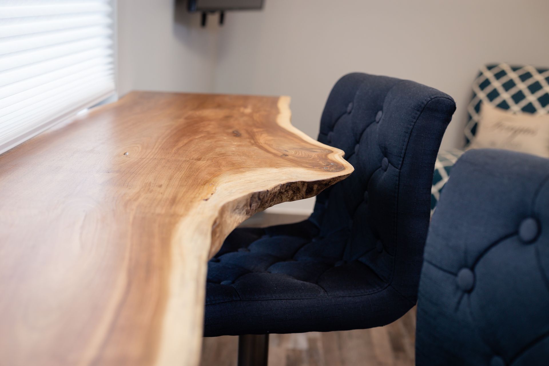 Close-up of a wooden live-edge counter with a blue tufted bar stool.