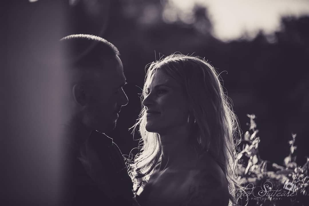Couple gazing at each other. The woman has blonde hair, backlight highlighting their profiles in a natural setting.