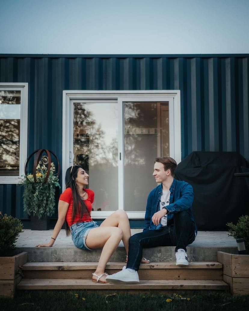 Couple sitting on steps in front of a blue house, smiling and talking outdoors.
