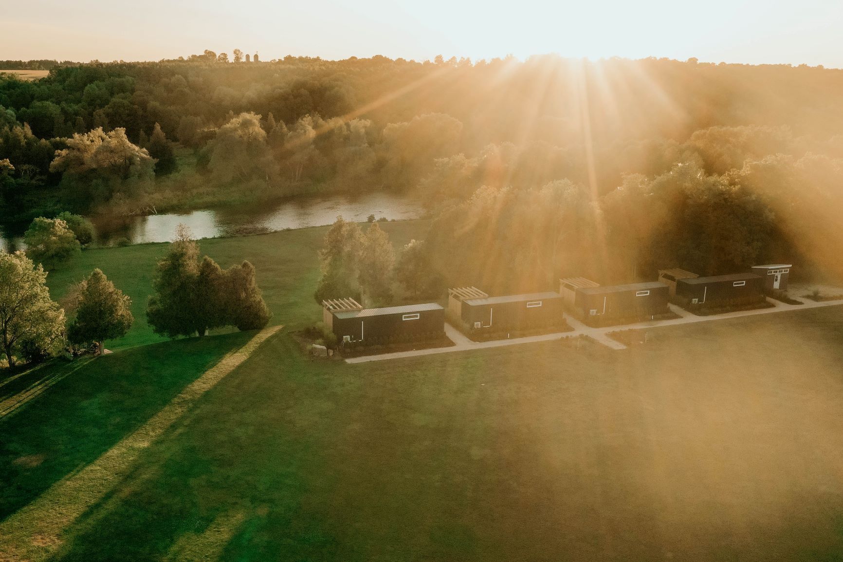 Sunset over a field with cabins and a pond, bathed in golden light.