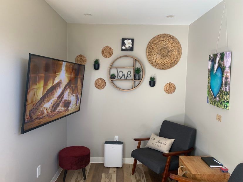 Cozy corner with TV, armchair, decorations, and small table. Neutral walls, wood floors, and an air purifier.