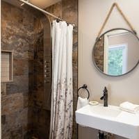 Shower with a gray, stone-like tile, white shower curtain, and round mirror hanging on the wall.