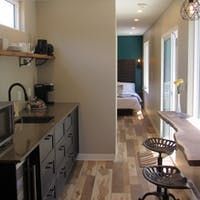 Kitchen with black cabinets, bar stools, and bedroom visible down the hall.
