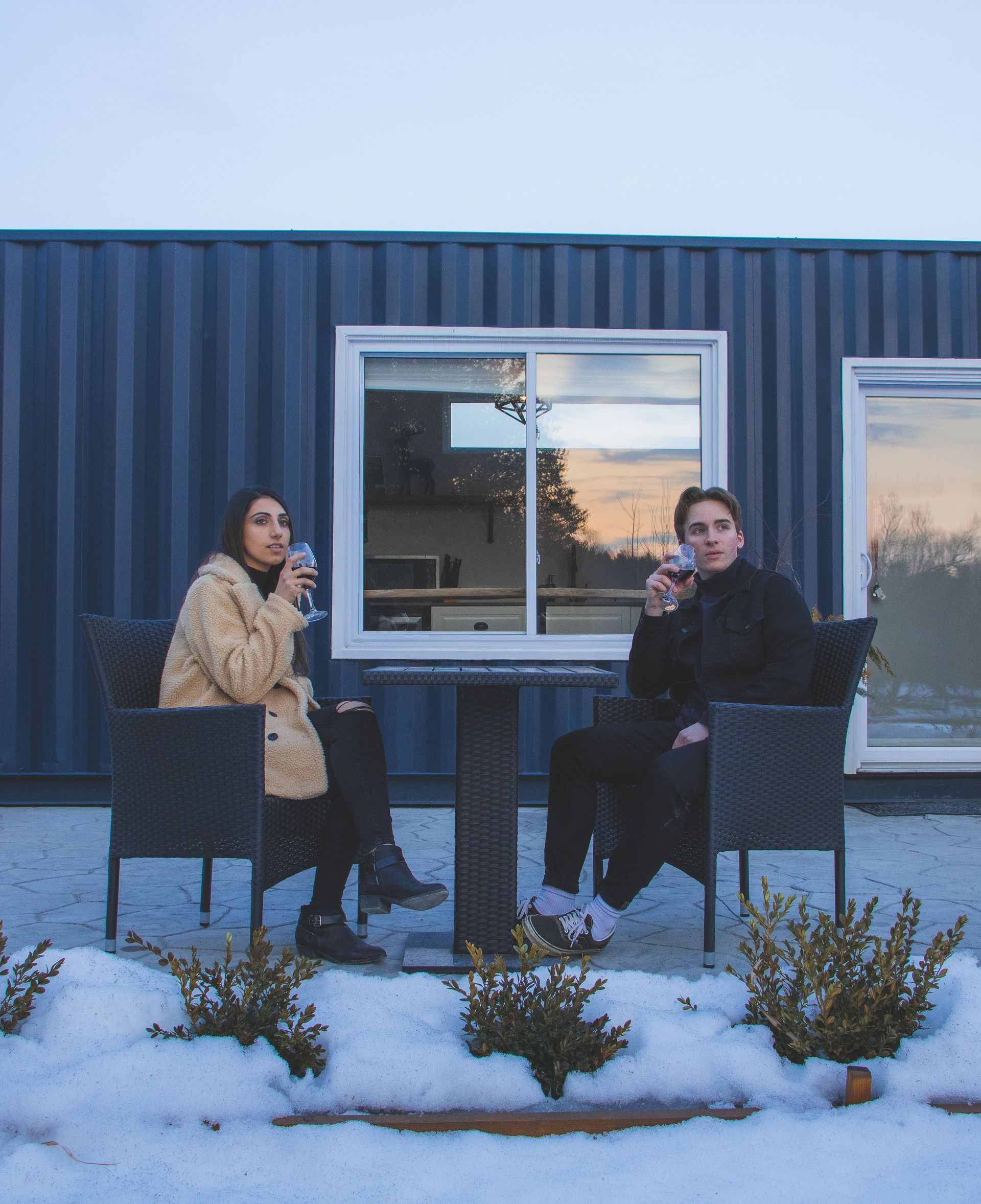 Two people drinking wine outside a blue shipping container. Snow on the ground.