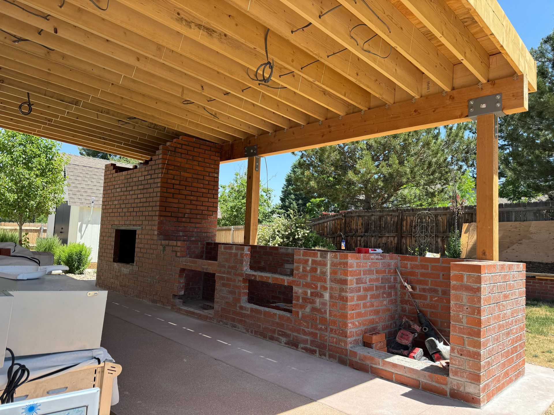 There is a wooden roof over a brick kitchen.