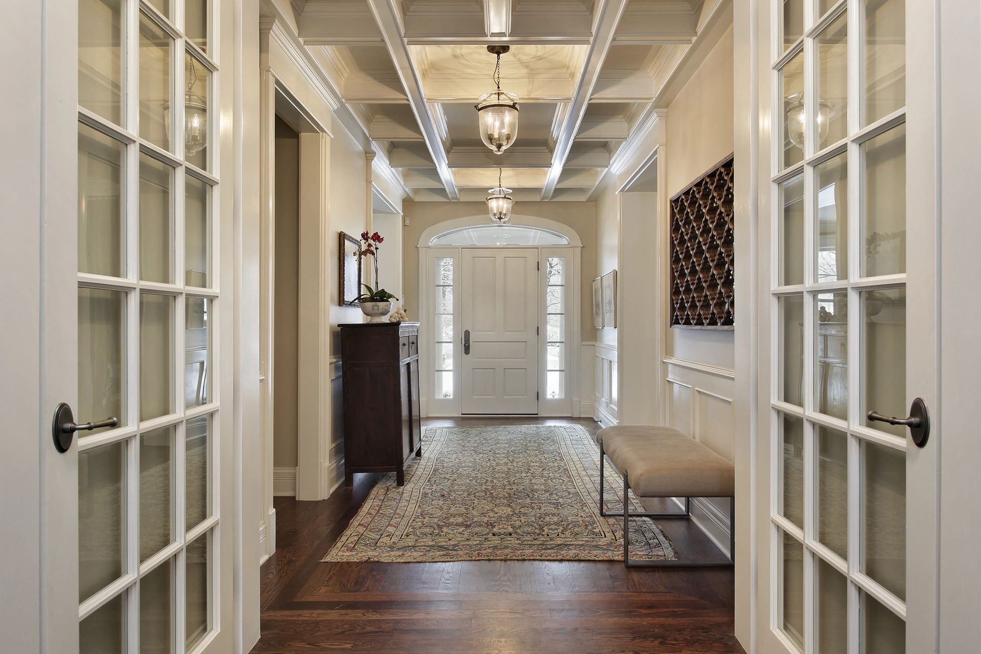 A hallway in a house with french doors and a bench.