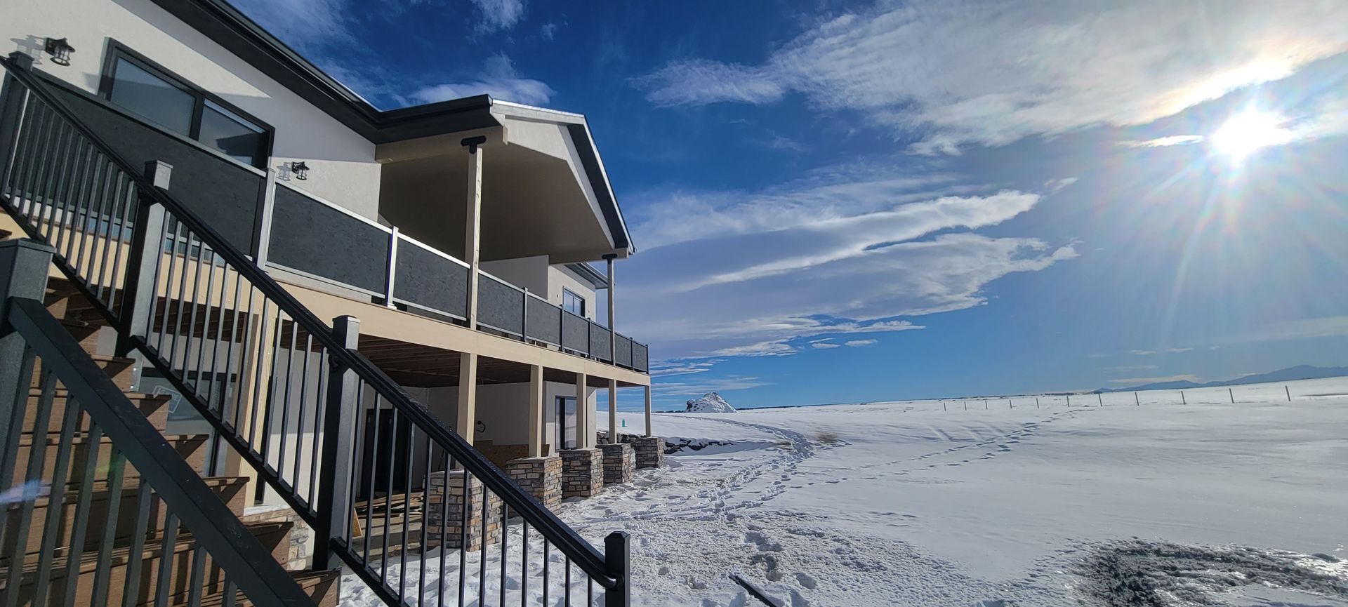 A house with a large deck and stairs leading up to it in the snow.