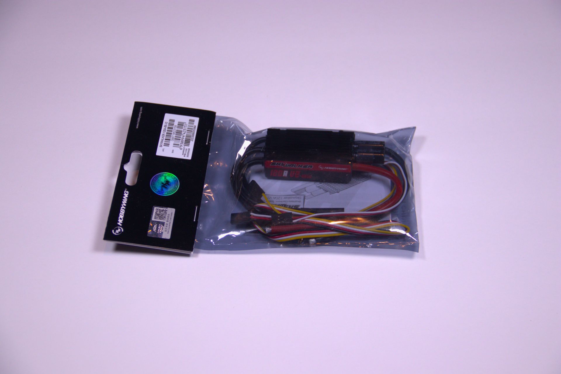 A packaged electronic component with visible wires inside a clear plastic bag with a black branding tag.