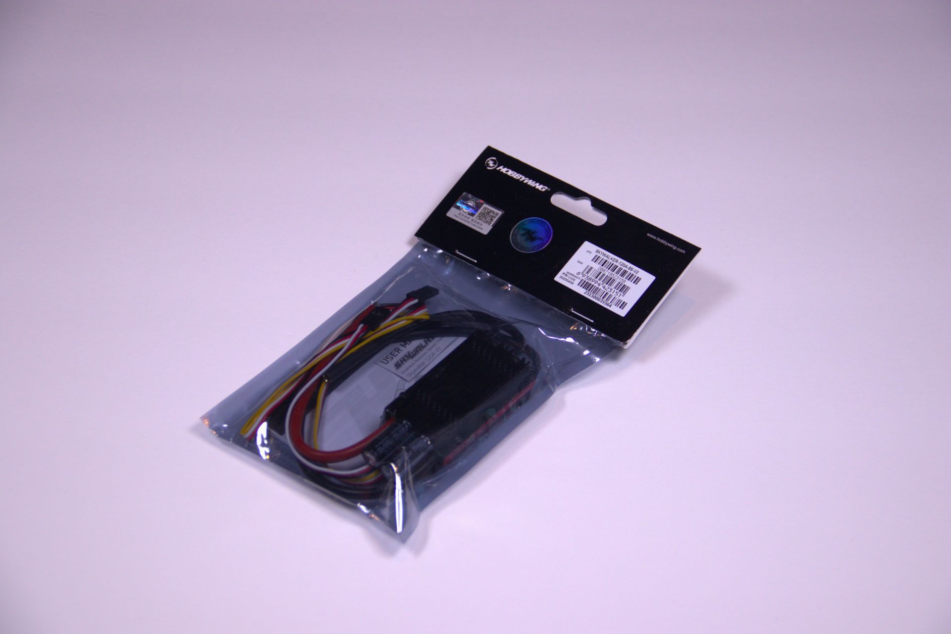 A packaged electronic component with visible wires inside a clear plastic bag with a black branding tag.