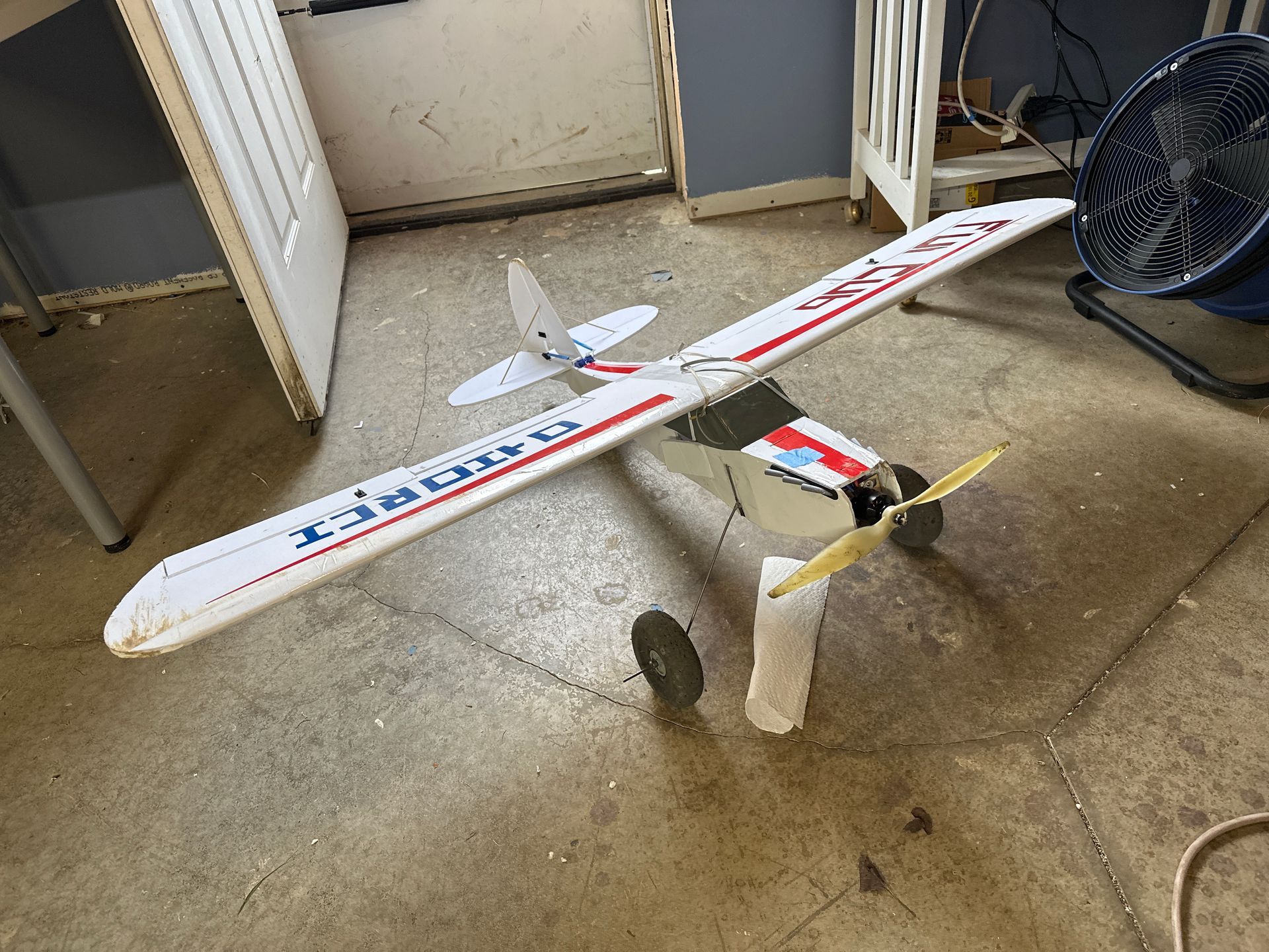 A small model airplane is sitting on the floor next to a fan.