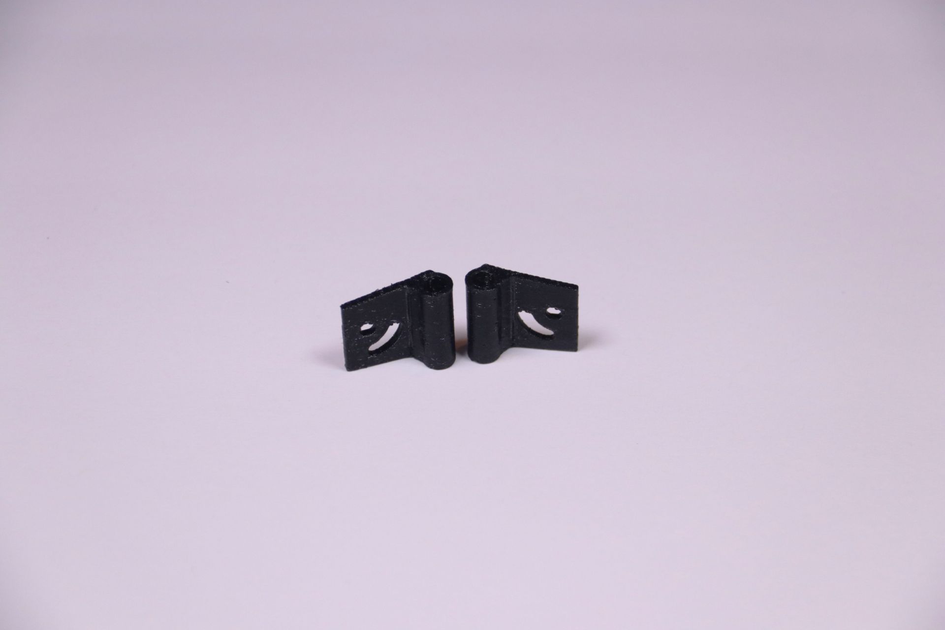 Two small black plastic clips on a light purple background