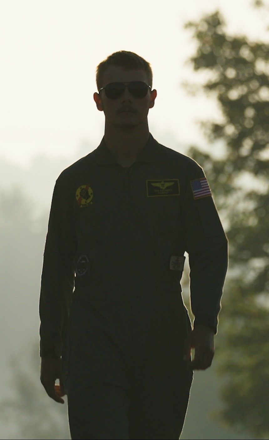 A man in a military uniform is holding a model airplane on a runway.