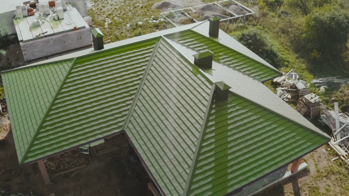 Green metal roof on a building with multiple sections and chimneys, aerial view.