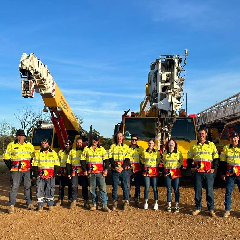 A Group Of Workers Are Posing For A Picture In Front Of A Crane — SureLift Crane Hire In Moranbah, QLD