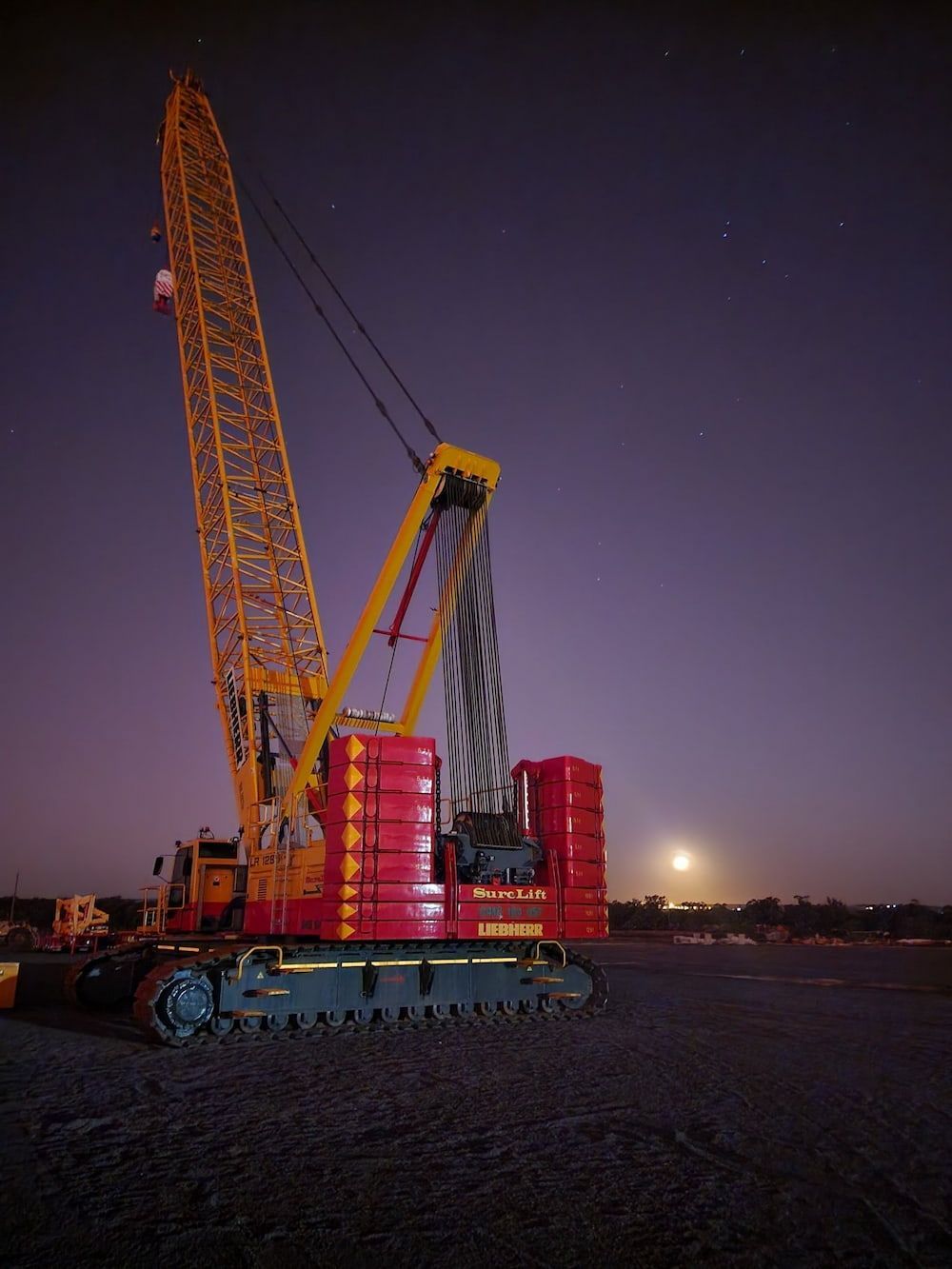 A Large Red And Yellow Crane Is Parked In A Dirt Field At Night — SureLift Crane Hire In Mackay, QLD