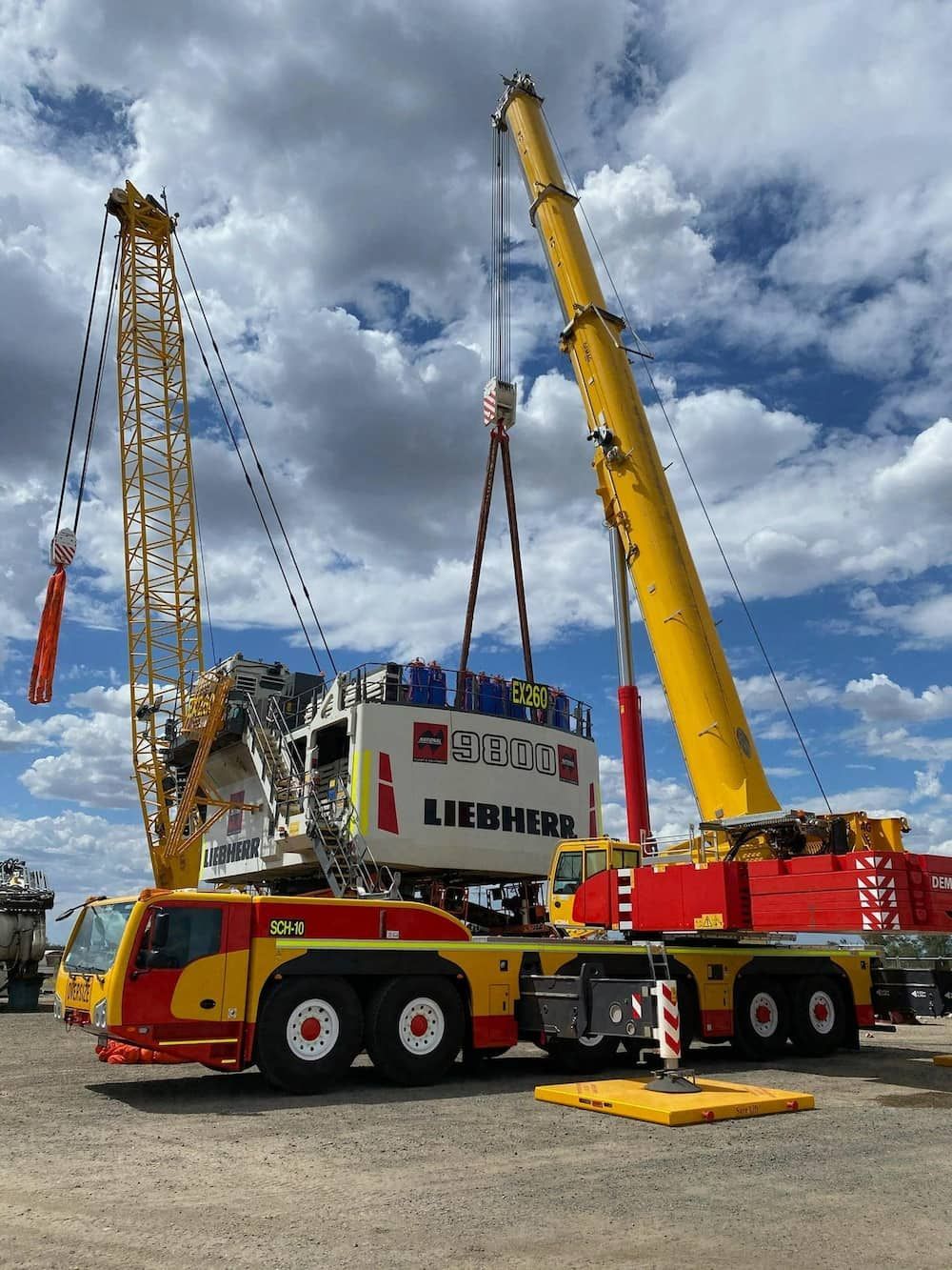A Yellow And Red Liebherr Truck Is Being Lifted By A Large Crane — SureLift Crane Hire In Moranbah, QLD