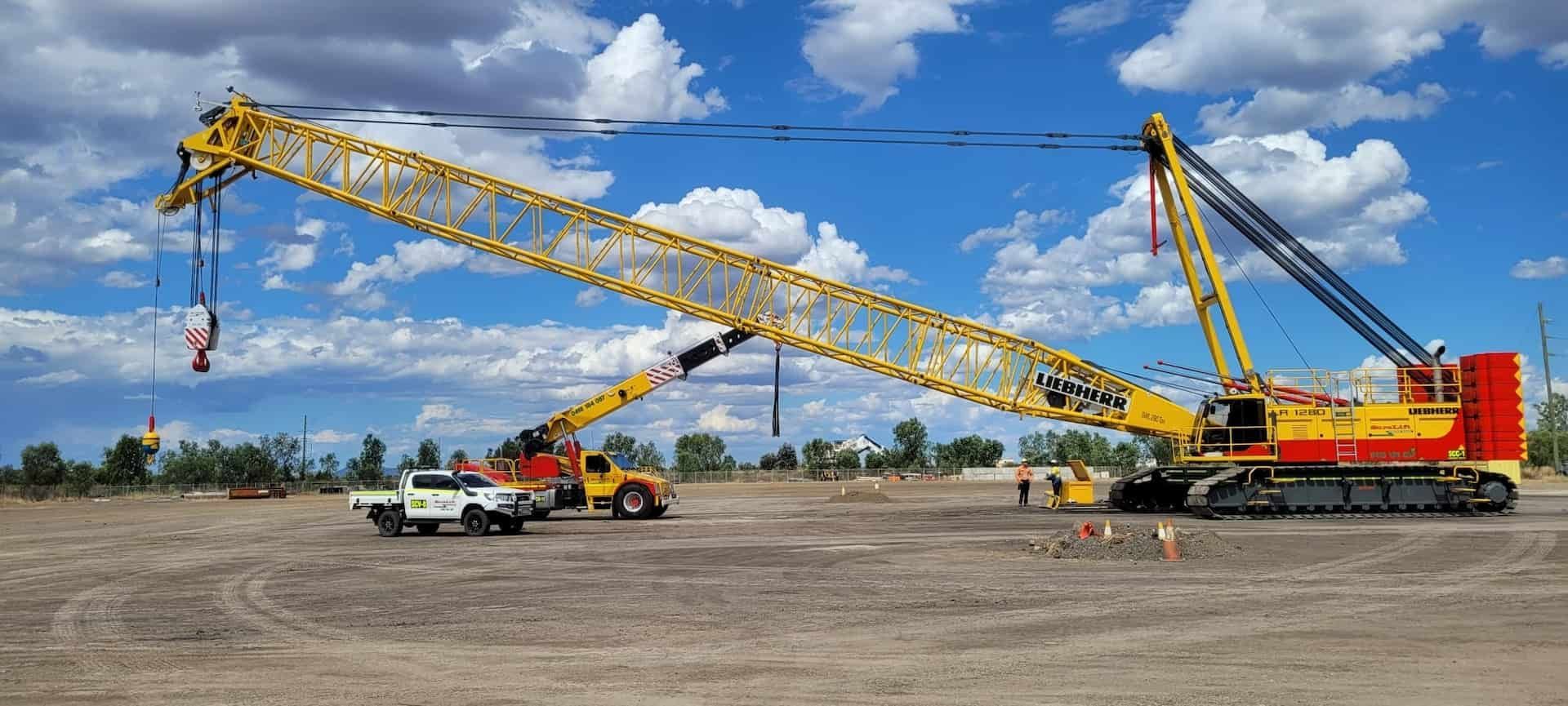 A Large Yellow Crane Is Parked In A Dirt Field Next To A Truck — SureLift Crane Hire In Mackay, QLD