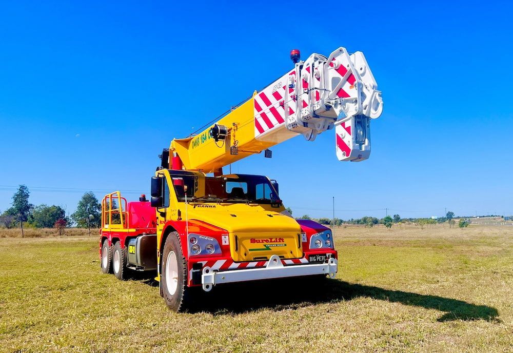 A Yellow And Red Crane Truck Is Parked In A Grassy Field — SureLift Crane Hire In Nebo, QLD
