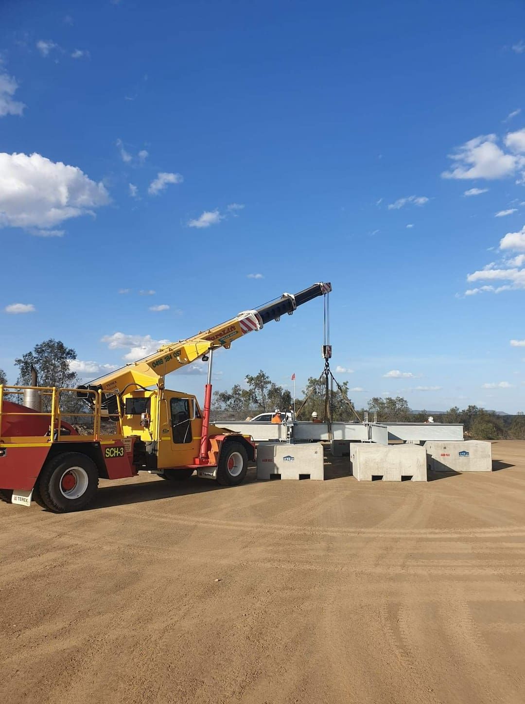 A Yellow Truck With A Crane Attached To It Is Parked In A Dirt Field — SureLift Crane Hire In Nebo, QLD