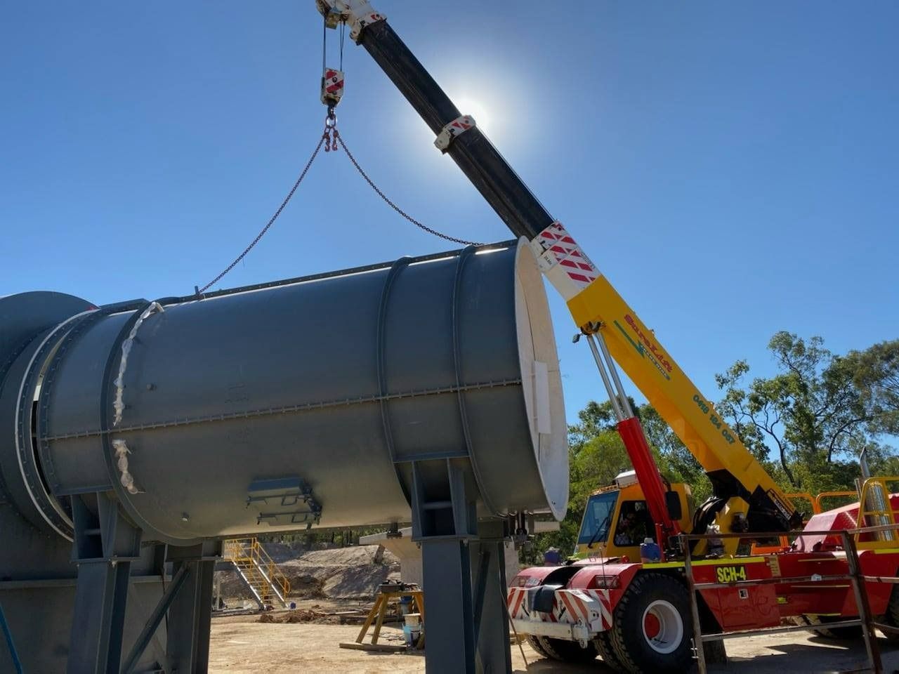 A Yellow Crane Is Lifting A Large Metal Object — SureLift Crane Hire In Moranbah, QLD