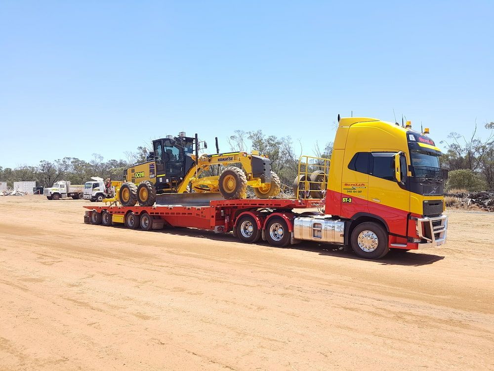 A Yellow And Red Semi Truck Is Carrying A Bulldozer On A Flatbed Trailer — SureLift Crane Hire In Moranbah, QLD