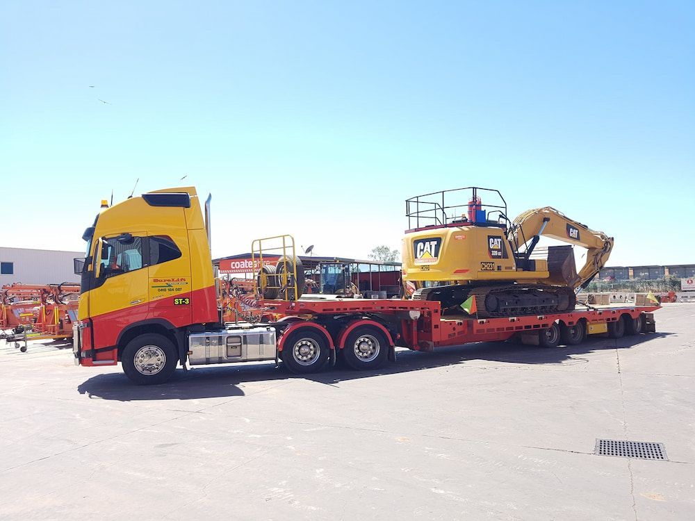 A Yellow And Red Truck Is Carrying A Cat Excavator On A Trailer — SureLift Crane Hire In Moranbah, QLD